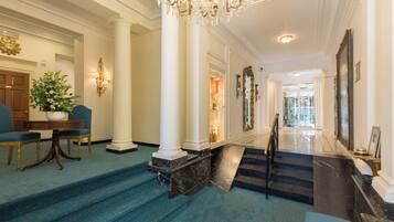 A grand lobby with marble steps, a chandelier, and a staircase leading to another area.
