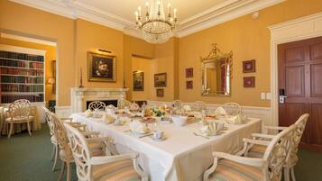 Un comedor formal con una larga mesa dispuesta para una comida, rodeada de sillas ornamentales.