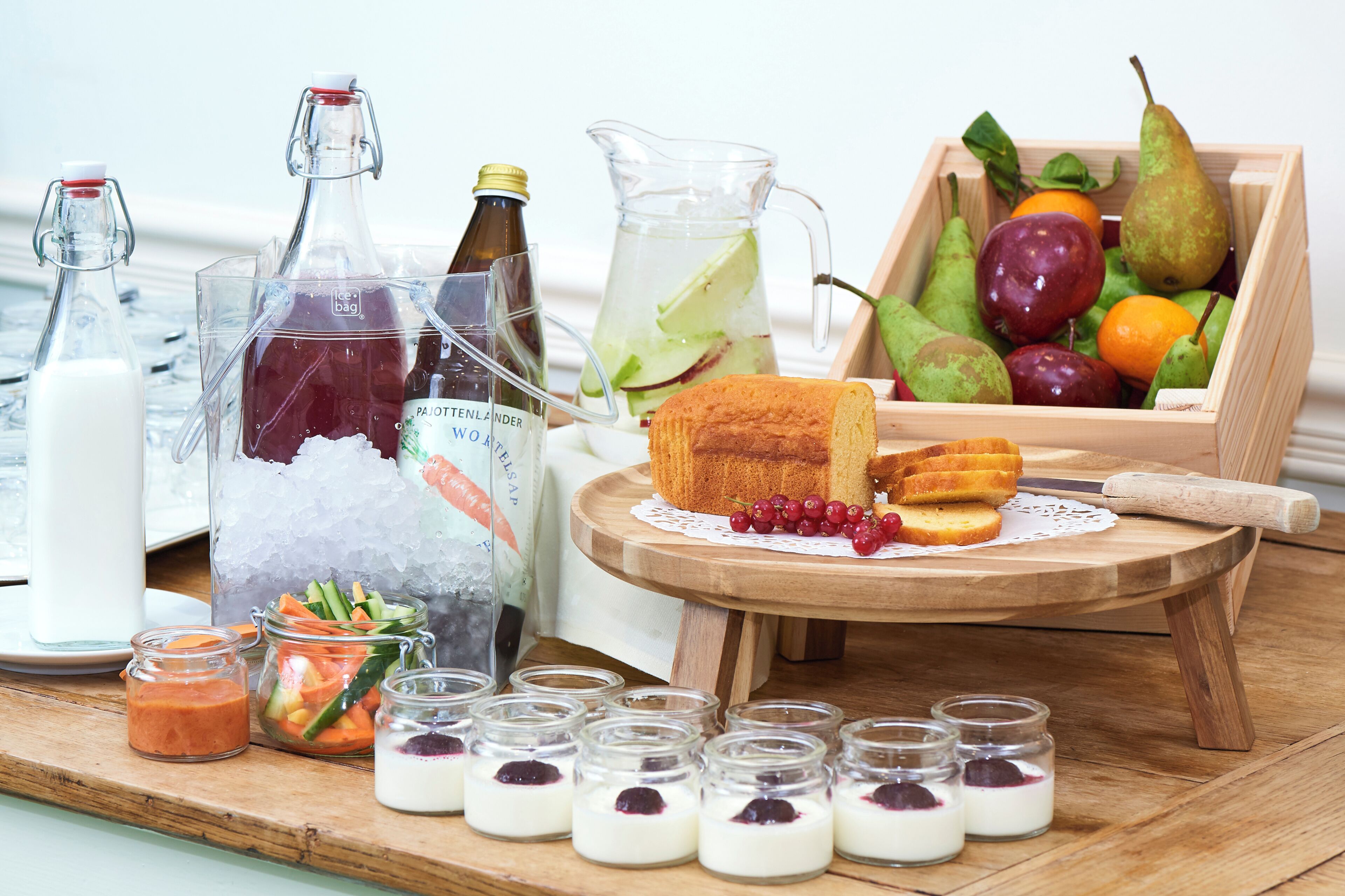 A wooden table with a variety of food items including bread, fruits, and jars of preserves.
