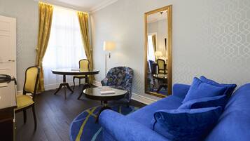 A hotel room with a blue sofa, a round table, a floral armchair, and a large mirror.