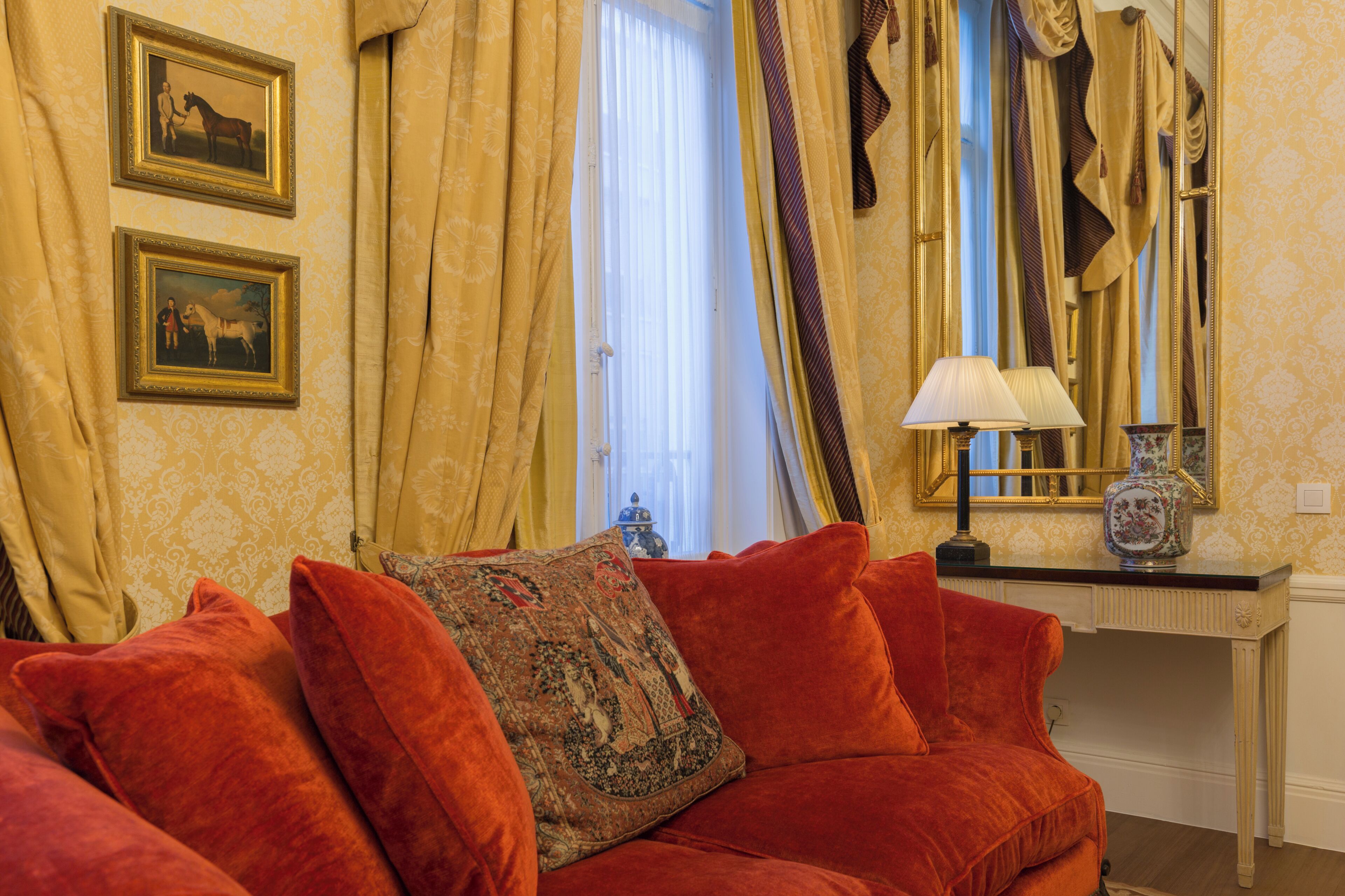 Una habitación con un sofá de terciopelo rojo, un cojín estampado, un espejo y dos cuadros en la pared.