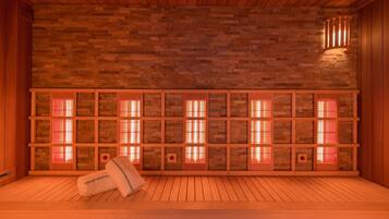 A sauna room with a wooden floor and a stone wall. There are several benches and a towel on the floor.