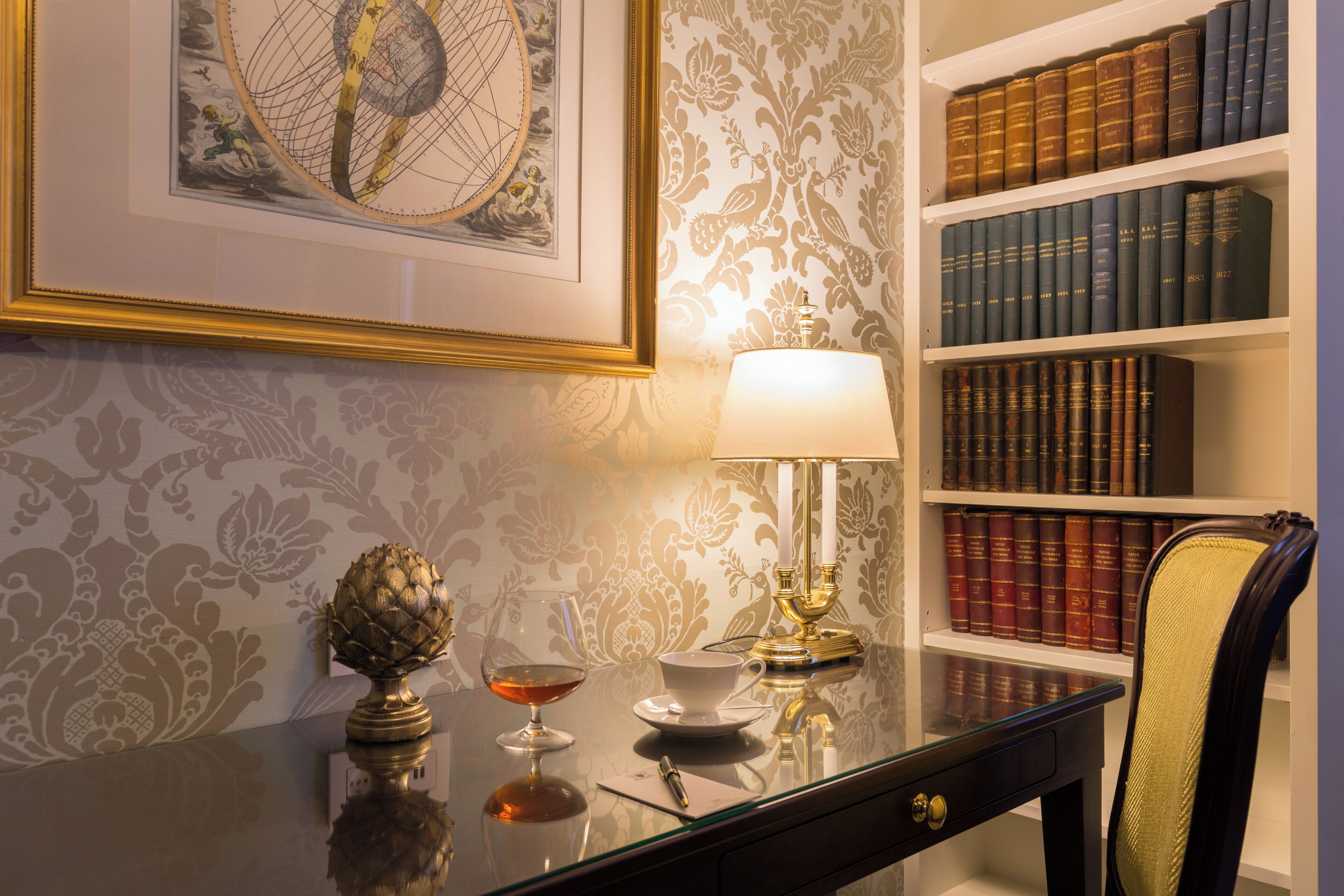 A study room with a desk, a lamp, a globe, and a bookshelf filled with books.
