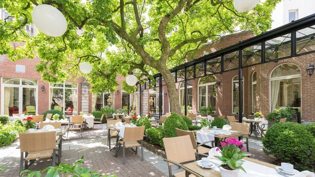 Eine Außenpatio-Terrasse mit Tischen und Stühlen, umgeben von Grünpflanzen und Ziegelmauern.