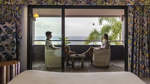 A room with a bed, a balcony with two chairs, and a view of the sea. - La Toubana Hôtel & Spa (Sainte-Anne)