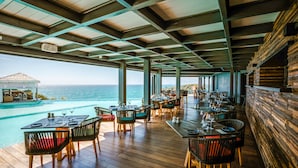 A restaurant with outdoor seating overlooking a pool and the ocean. - La Toubana Hôtel & Spa (Sainte-Anne)