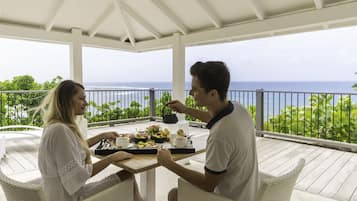 Un espacio de comedor al aire libre cubierto con vistas al océano, con una mesa dispuesta con comida y bebidas.