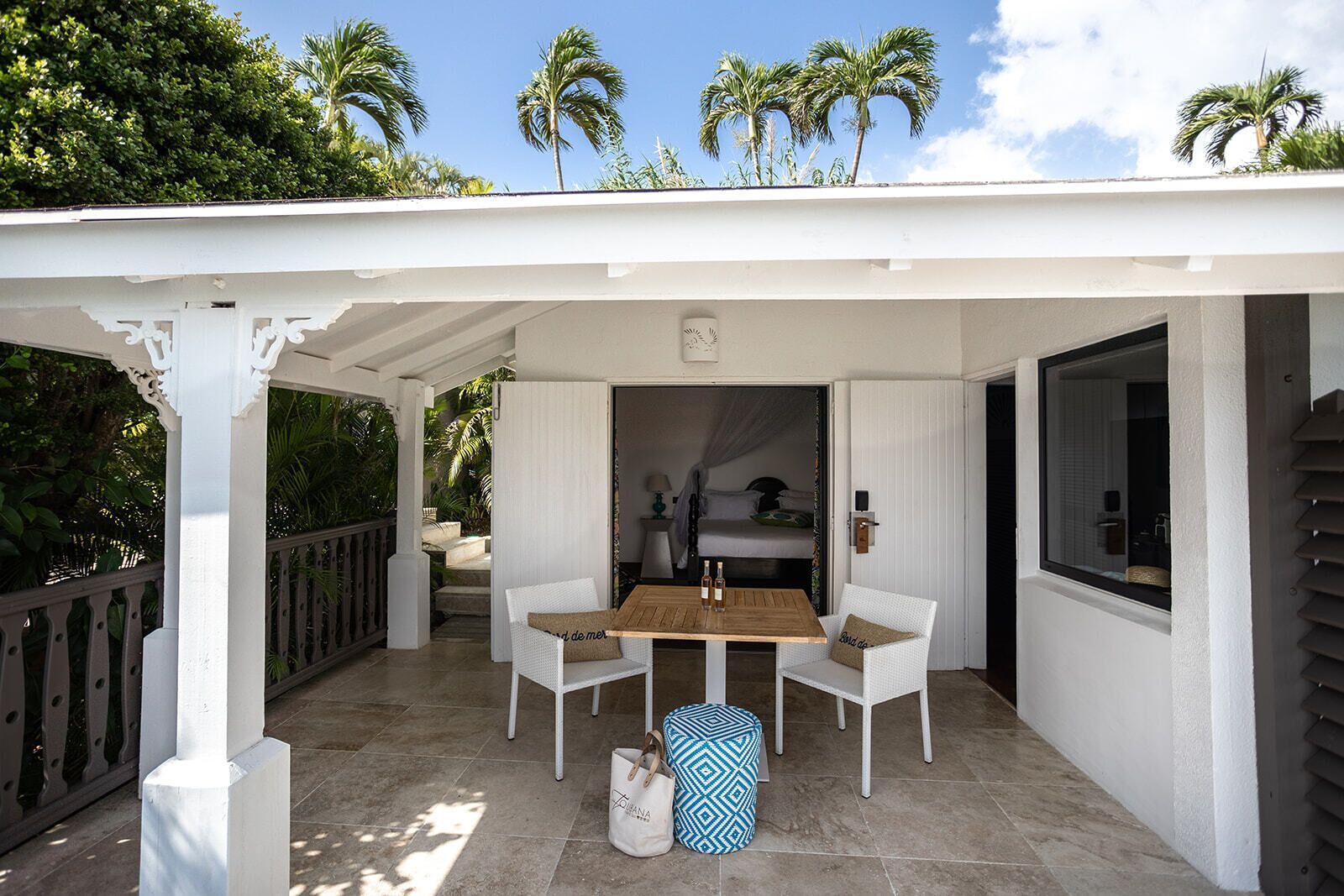 A covered patio with a table and chairs, a bed with a canopy, and a view of palm trees.