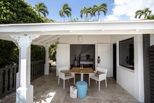 Un patio cubierto con una mesa y sillas, una cama con dosel, y vistas a palmeras.