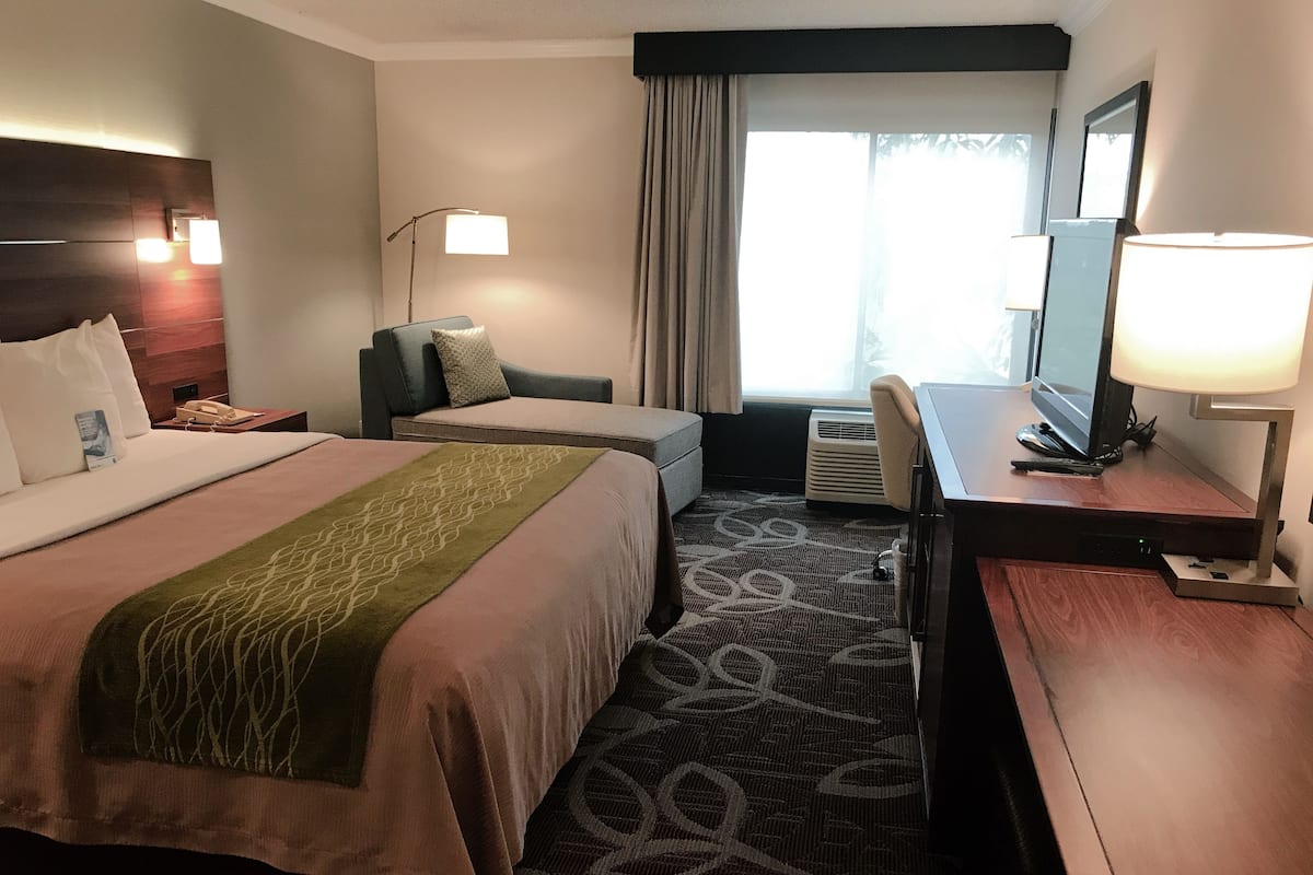 A hotel room with two beds, a desk, a chair, a television, and a window with curtains.
