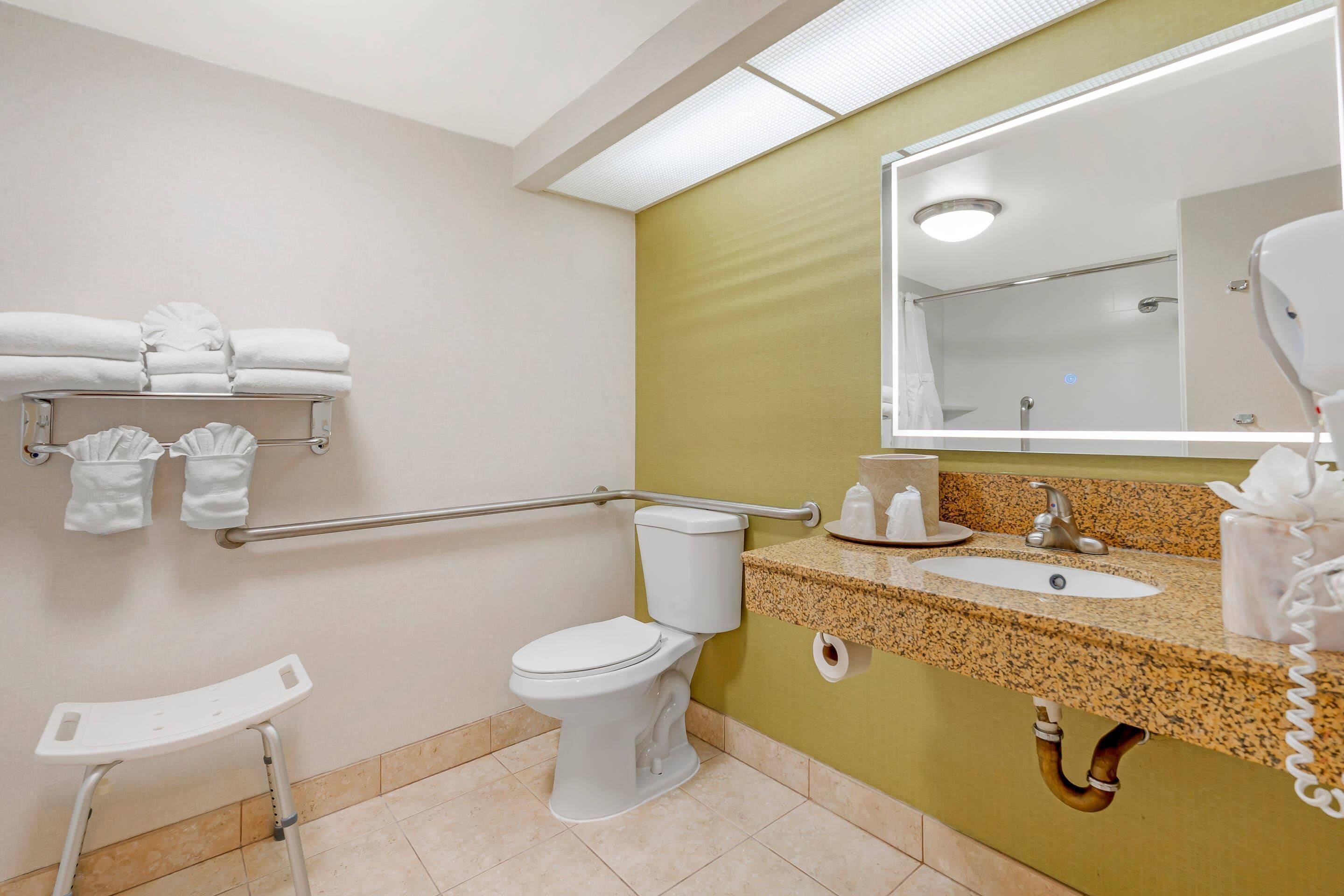 A bathroom with a white toilet, a sink with a granite countertop, a mirror, and a towel rack with folded towels.