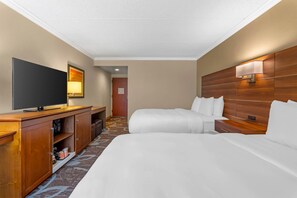 Habitación de hotel con un televisor de pantalla plana grande, cabecera de madera, mesita de noche y piso alfombrado.