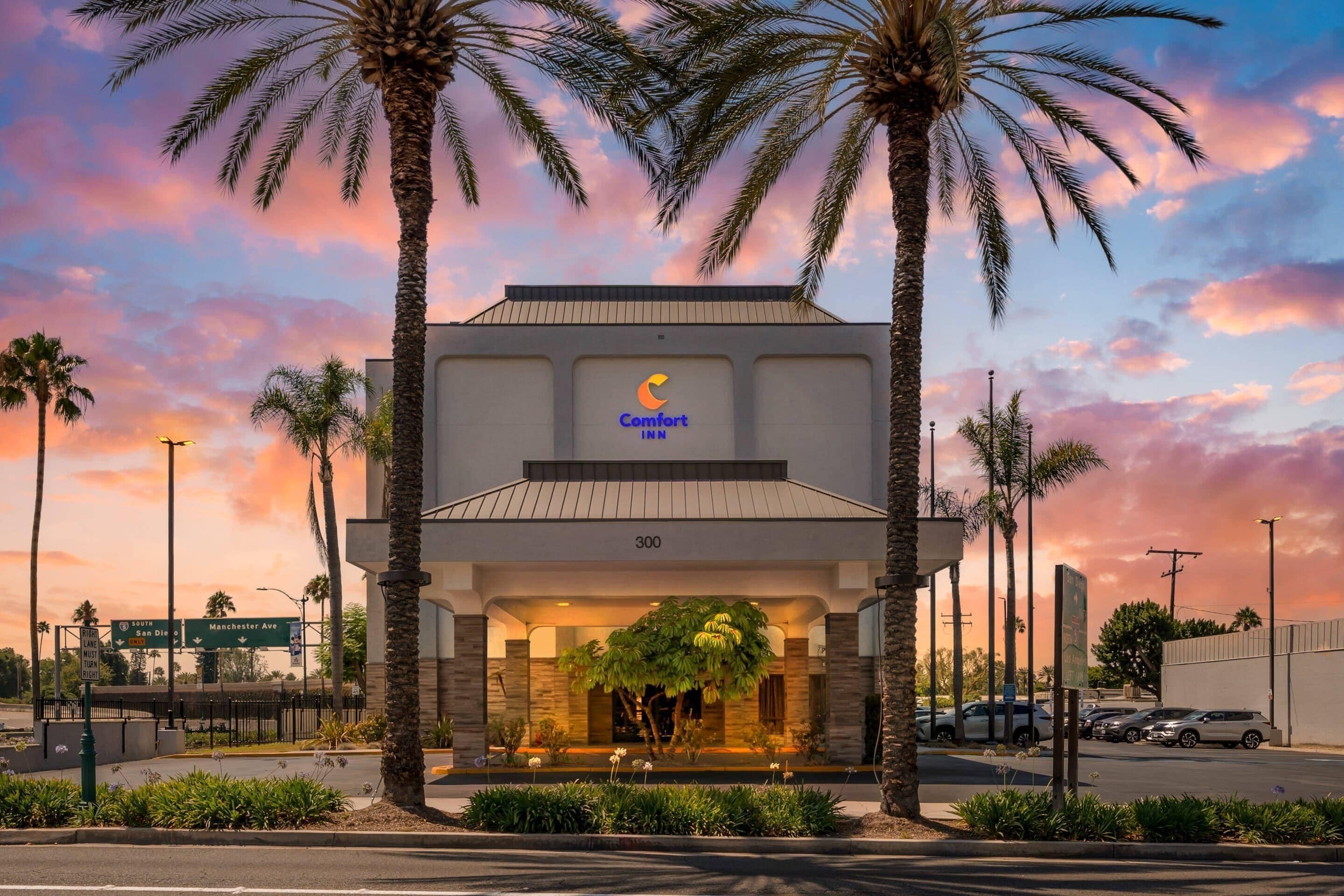 Een Comfort Inn hotel met een moderne gevel, palmbomen en een zonsondergang.