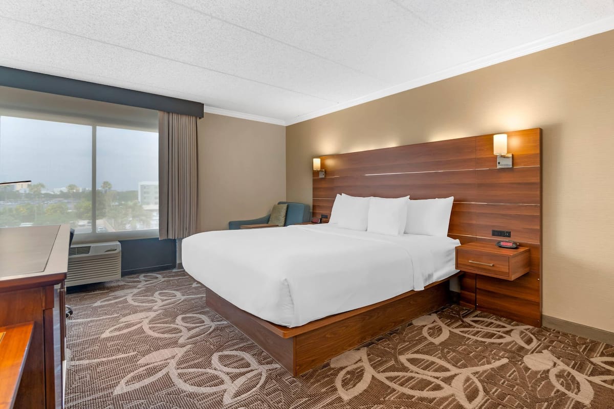 A hotel room with a large bed, a desk, a chair, and a window with a view of buildings.