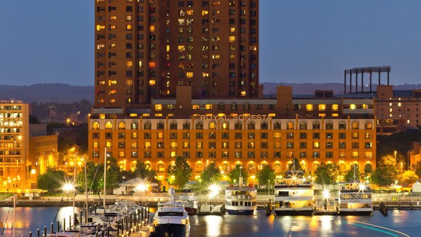 Hotel aan het water met meerdere verdiepingen, een jachthaven met boten en een stadsachtergrond.