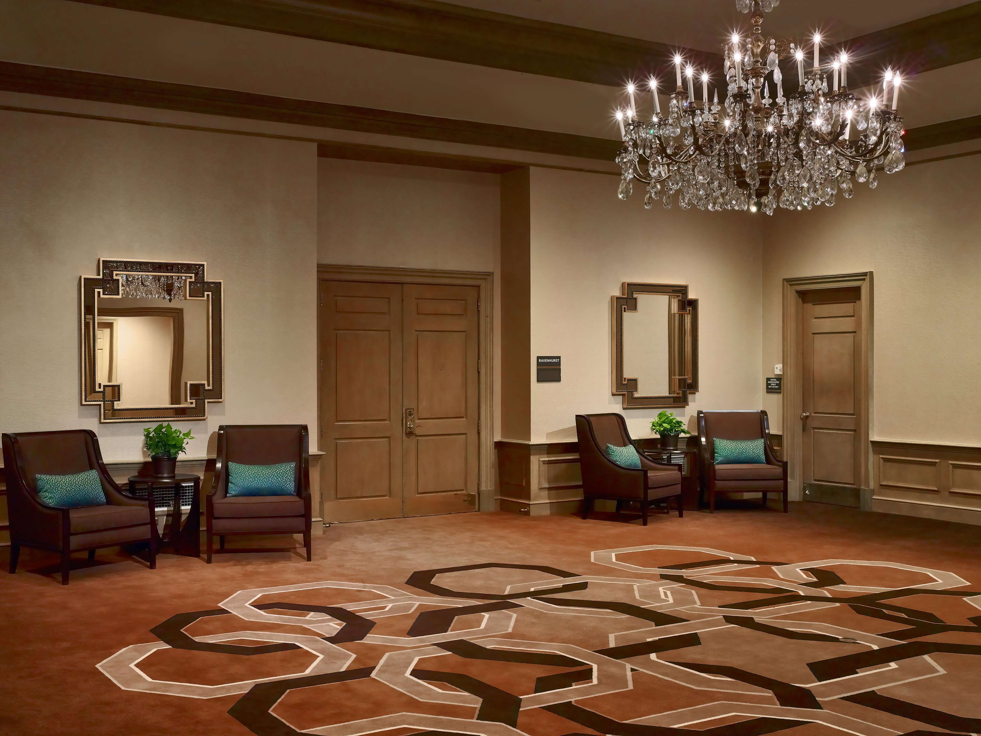 Un hall d’hôtel agrémenté d’un lustre, de deux grands miroirs, de portes en bois et d’un tapis à motifs.