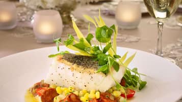 A white plate with a fish fillet, corn, cherry tomatoes, and greens.
