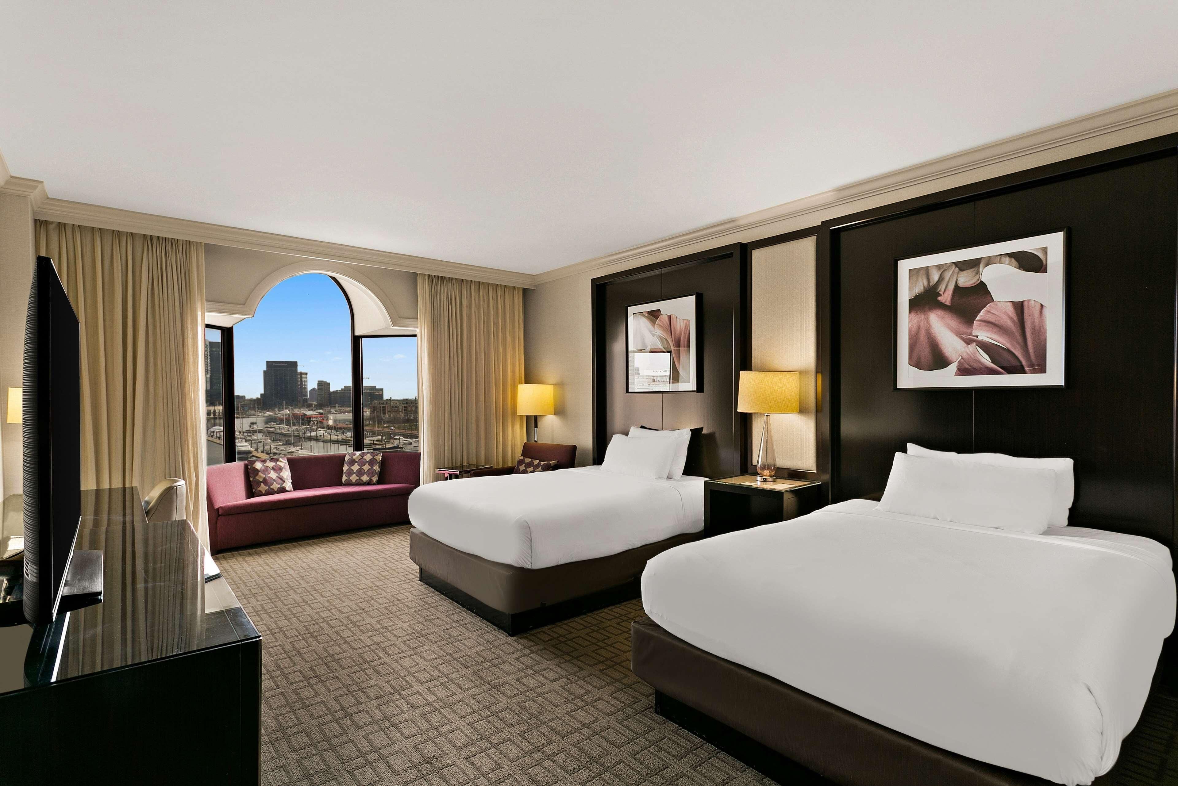Une chambre d’hôtel avec deux lits, un canapé, une télévision et une vue sur la ville.