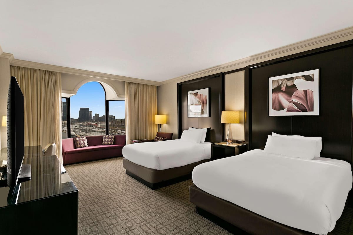 A hotel room with two beds, a sofa, a TV, and a city view.