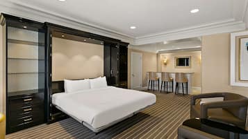 Una habitación de hotel con una cama grande, un escritorio con dos sillas, un minibar y un baño con ducha e inodoro.