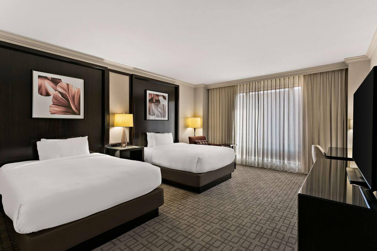 A hotel room with two beds, a desk, a TV, and two lamps.