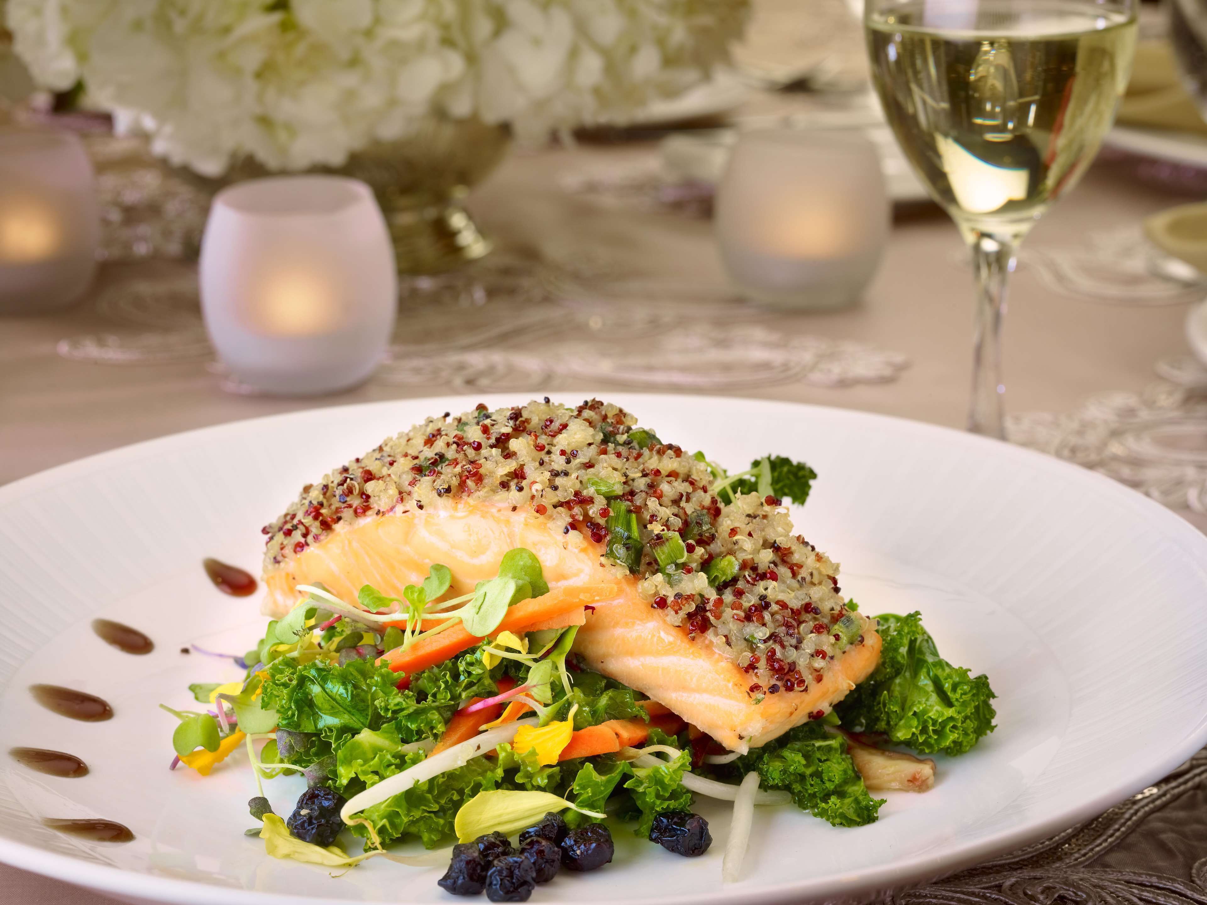 Une assiette de saumon accompagné de quinoa et de légumes verts, servie avec un verre de vin blanc.