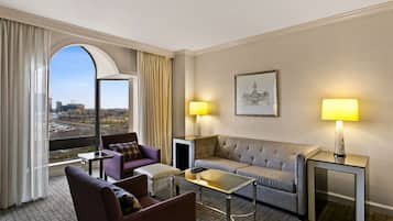 Habitación de hotel con un ventanal grande, un sofá, una silla, una mesita y dos lámparas.