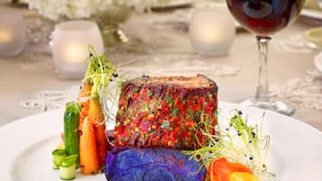 A plated dish with a steak topped with a colorful herb mixture, accompanied by vegetables and a glass of red wine.