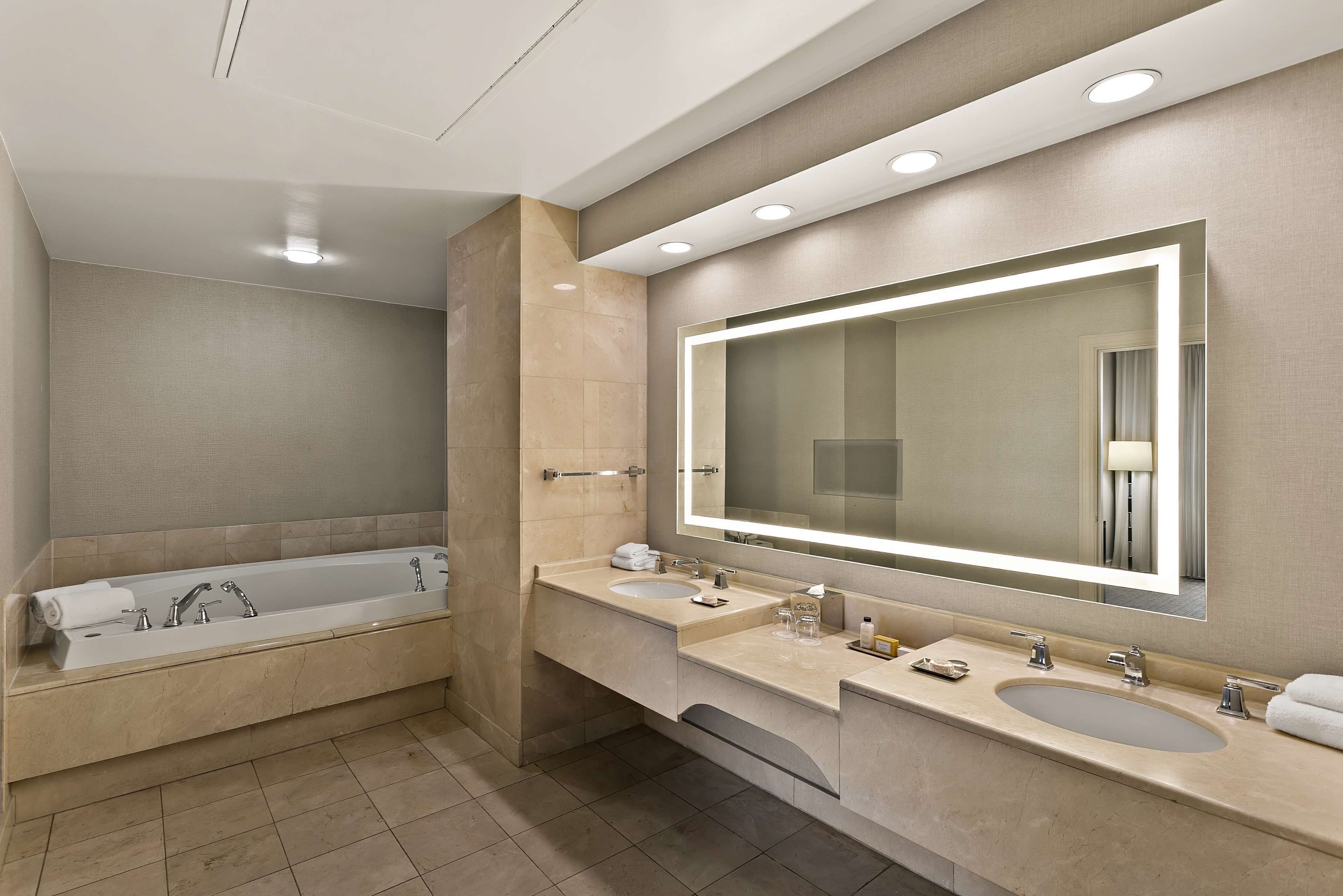 A modern bathroom with a bathtub, two sinks, and a large mirror.