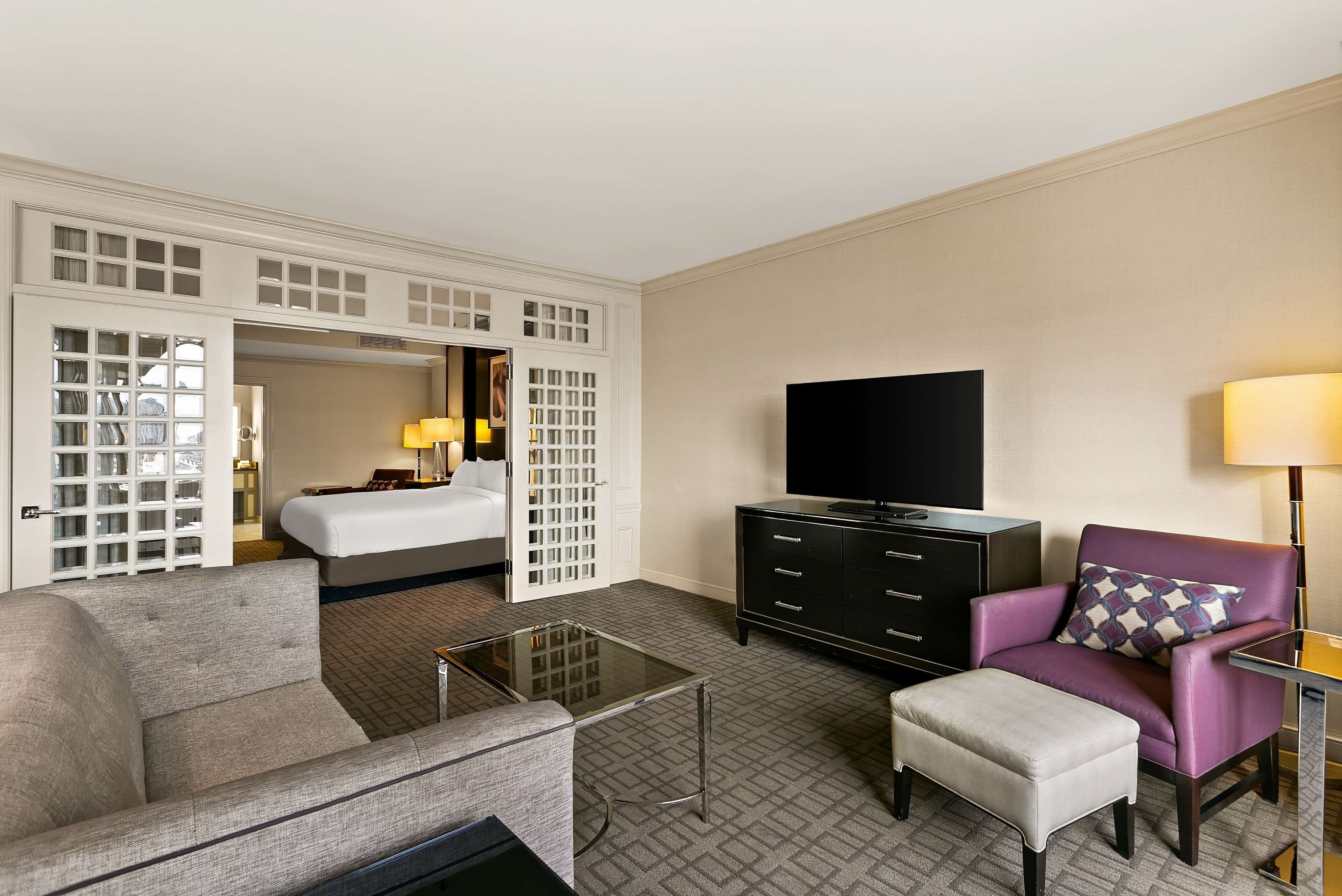 A hotel room with a sofa, a small table, a TV, a cabinet, and a bed.