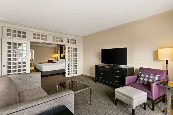 Una habitación de hotel con sofá, una mesa pequeña, televisor, armario y cama.