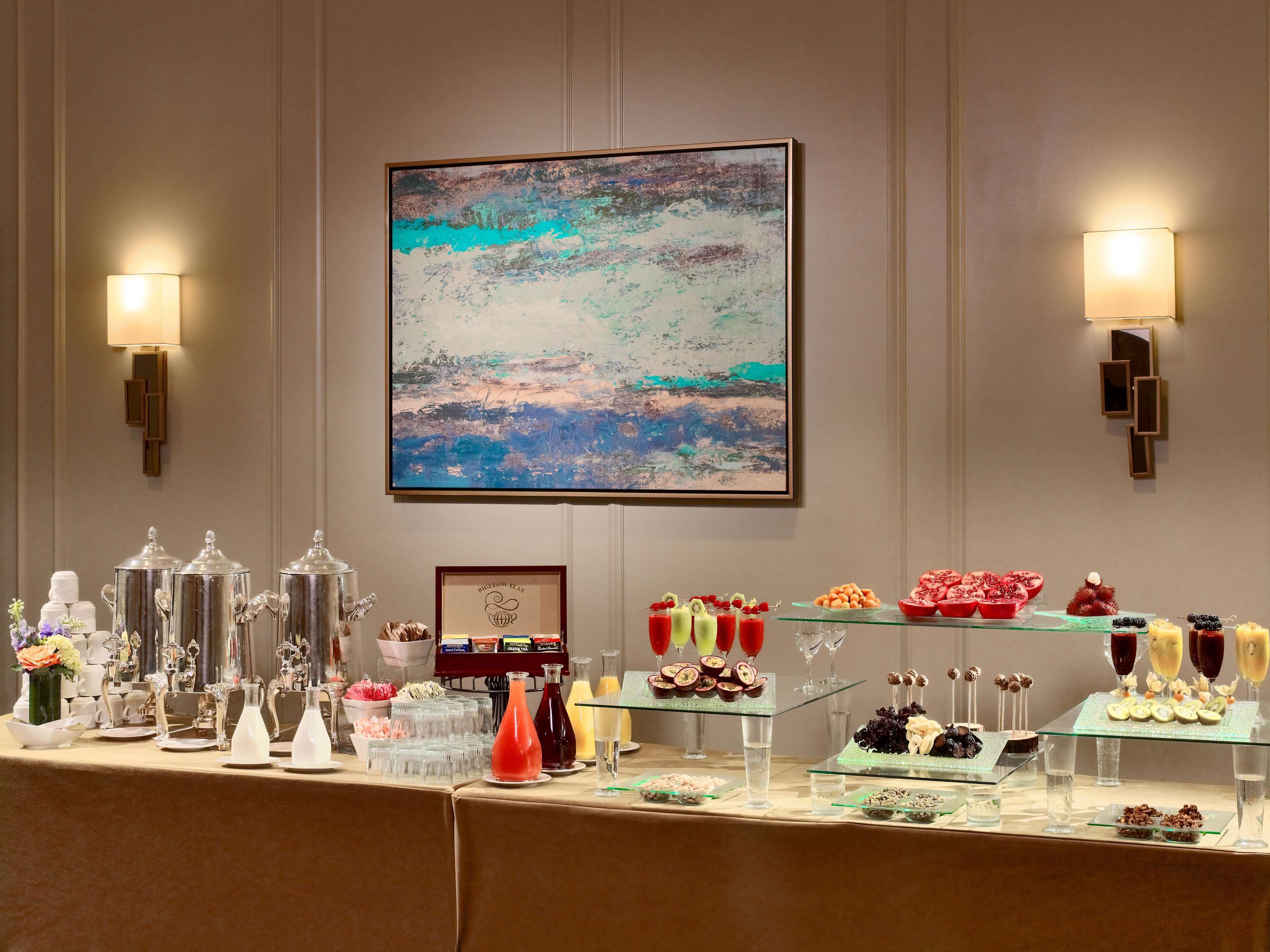 A buffet table with various food items and drink dispensers, a framed abstract painting on the wall, and wall-mounted sconces.