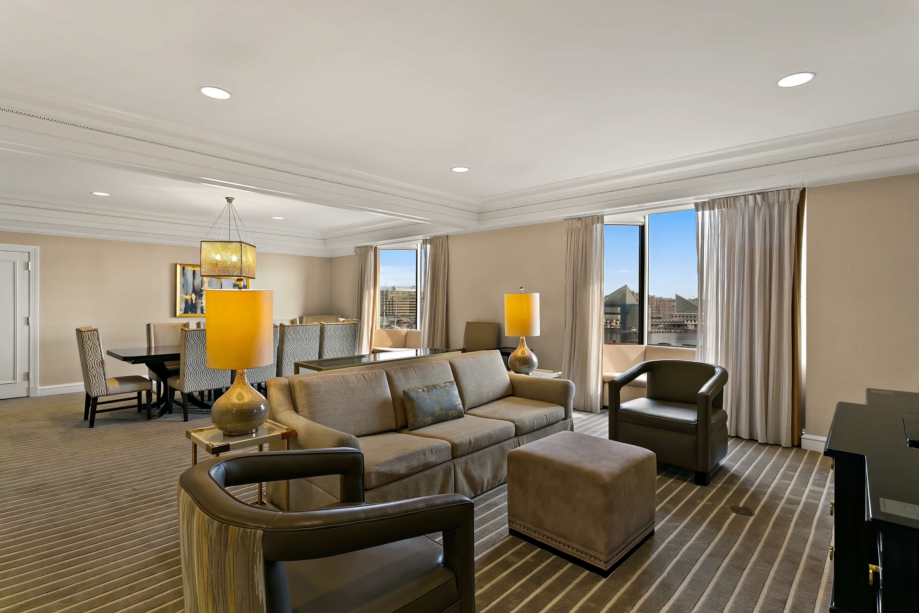 Una habitación de hotel con un sofá grande, una silla, una mesa de comedor con sillas y un televisor.