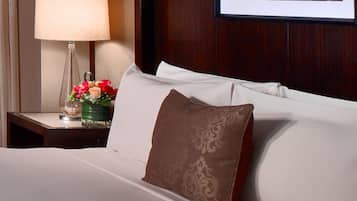 Una habitación de hotel con una cama, una mesita de noche con una lámpara y flores, y un cuadro en la pared.