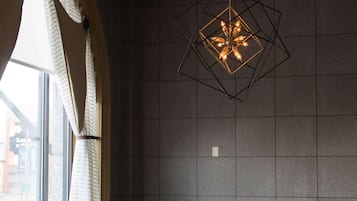 Comedor con una mesa dispuesta para seis comensales, una lámpara colgante de diseño geométrico y vistas a través de una ventana con cortinas.