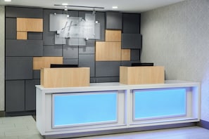 A reception desk with a modern design, featuring a combination of wood and grey panels, and illuminated blue panels on the front.