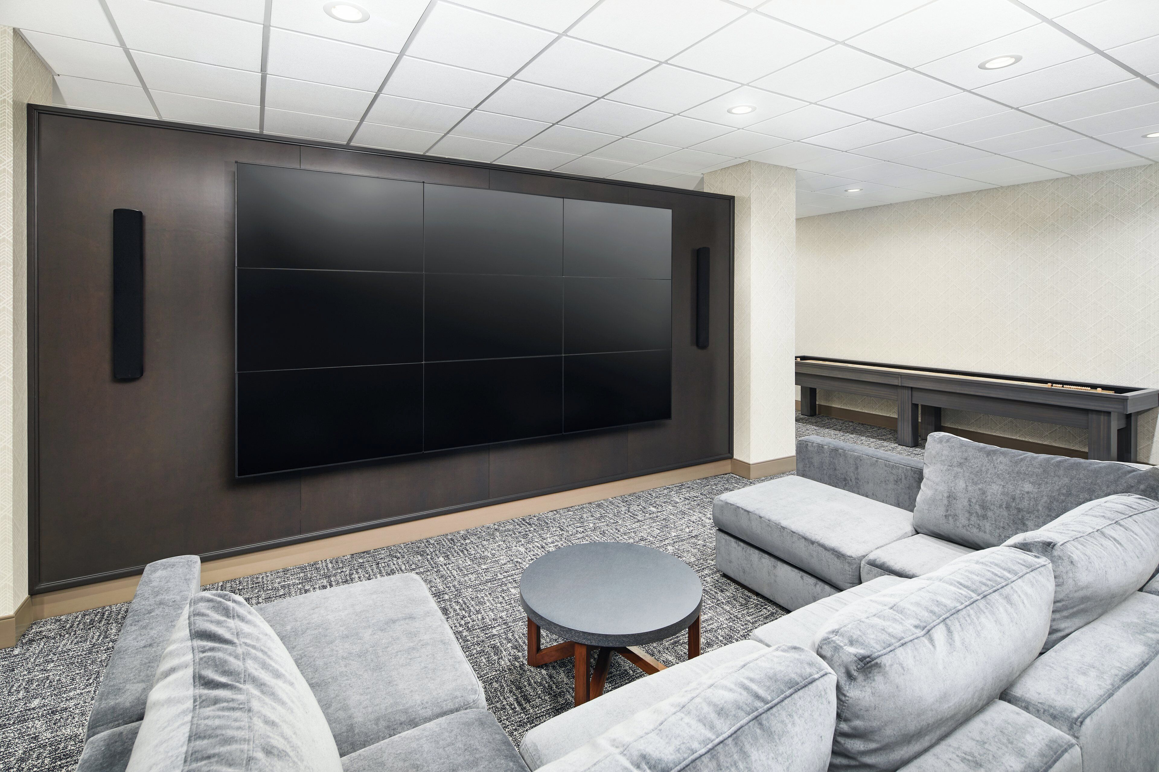 A modern living room with a large flat-screen TV, grey sofas, and a small round table.