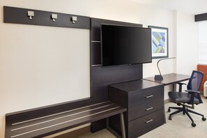 A modern office space with a large flat-screen TV mounted on a dark wall, a desk with a chair, and a bench.