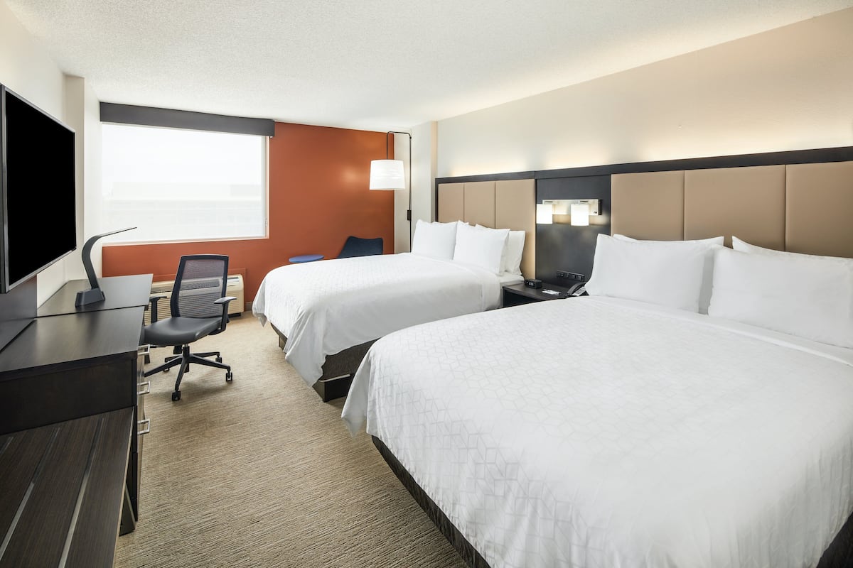 A hotel room with two beds, a desk, a chair, a TV, and a window.