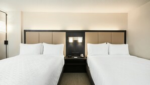 Une chambre d’hôtel avec deux lits, une table de chevet avec un téléphone et une lampe, et une tête de lit dotée d’un éclairage intégré.