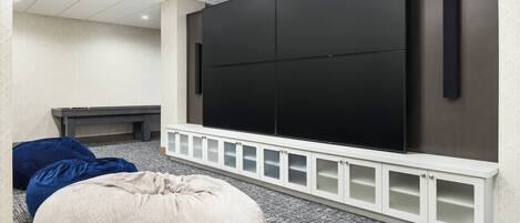 A modern living room with a large flat-screen TV, a white entertainment unit, and two bean bags.