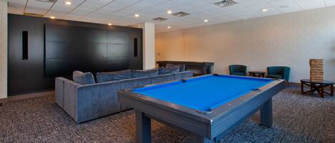 A pool table in a room with a carpeted floor, a sofa, and a small table with chairs.