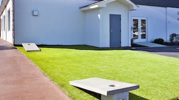 Un edificio moderno con tetto piatto, un piccolo ingresso e un prato ben curato con due panchine in cemento.