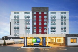 A multi-story hotel with a prominent red and white facade, a Holiday Inn Express sign, and a parking lot with a 'No Parking' sign.
