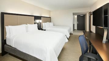 Habitación de hotel con dos camas, un escritorio, una silla, un televisor y una puerta que da a otra habitación.