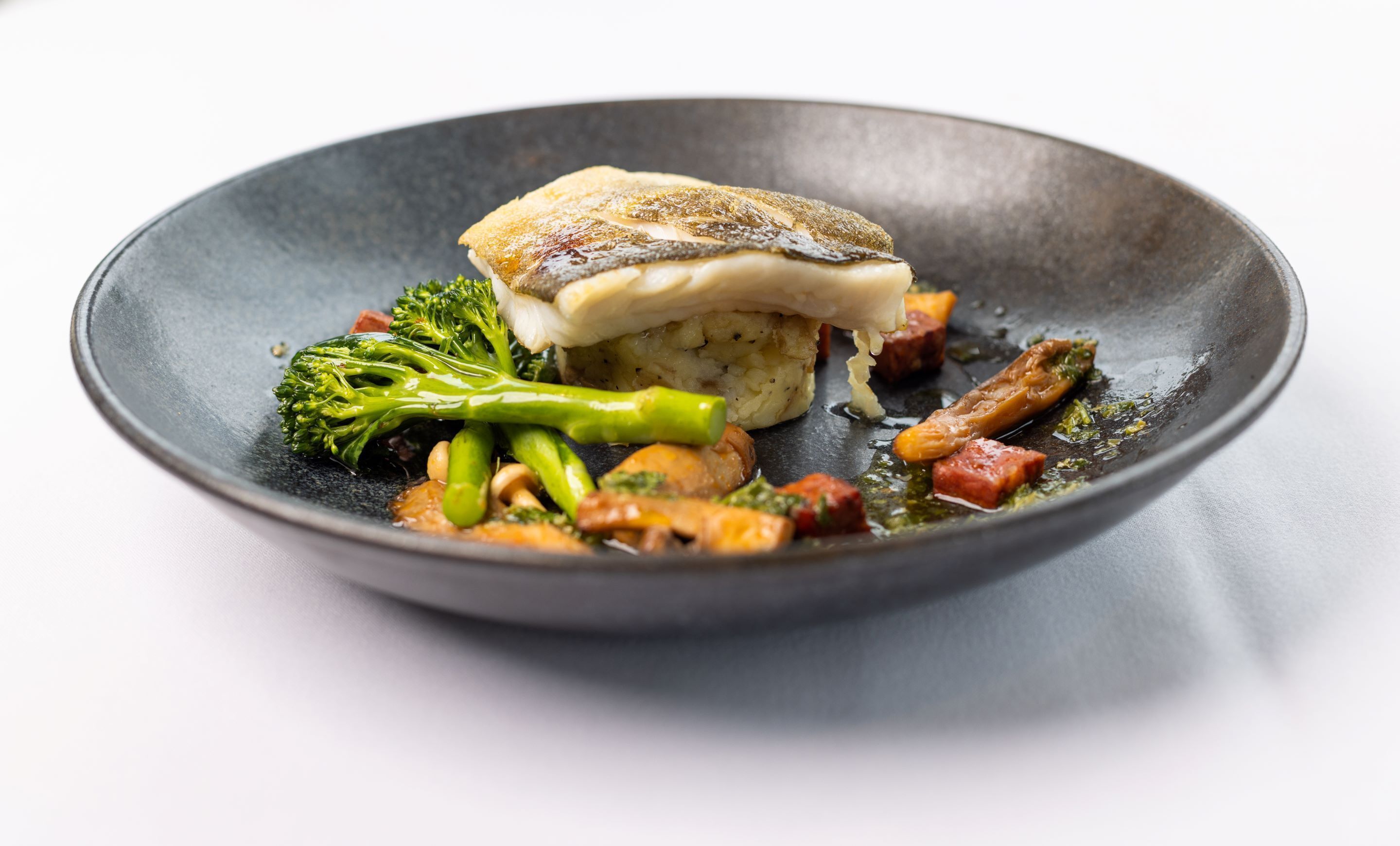 Un piatto con un filetto di pesce, broccoli e altre verdure.