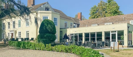 A courtyard with a gravel area, a neatly trimmed hedge, and a building with a large windowed section.
