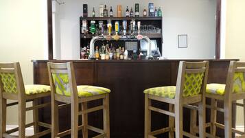 A bar area with a wooden counter, multiple liquor bottles, and two chairs with patterned cushions.