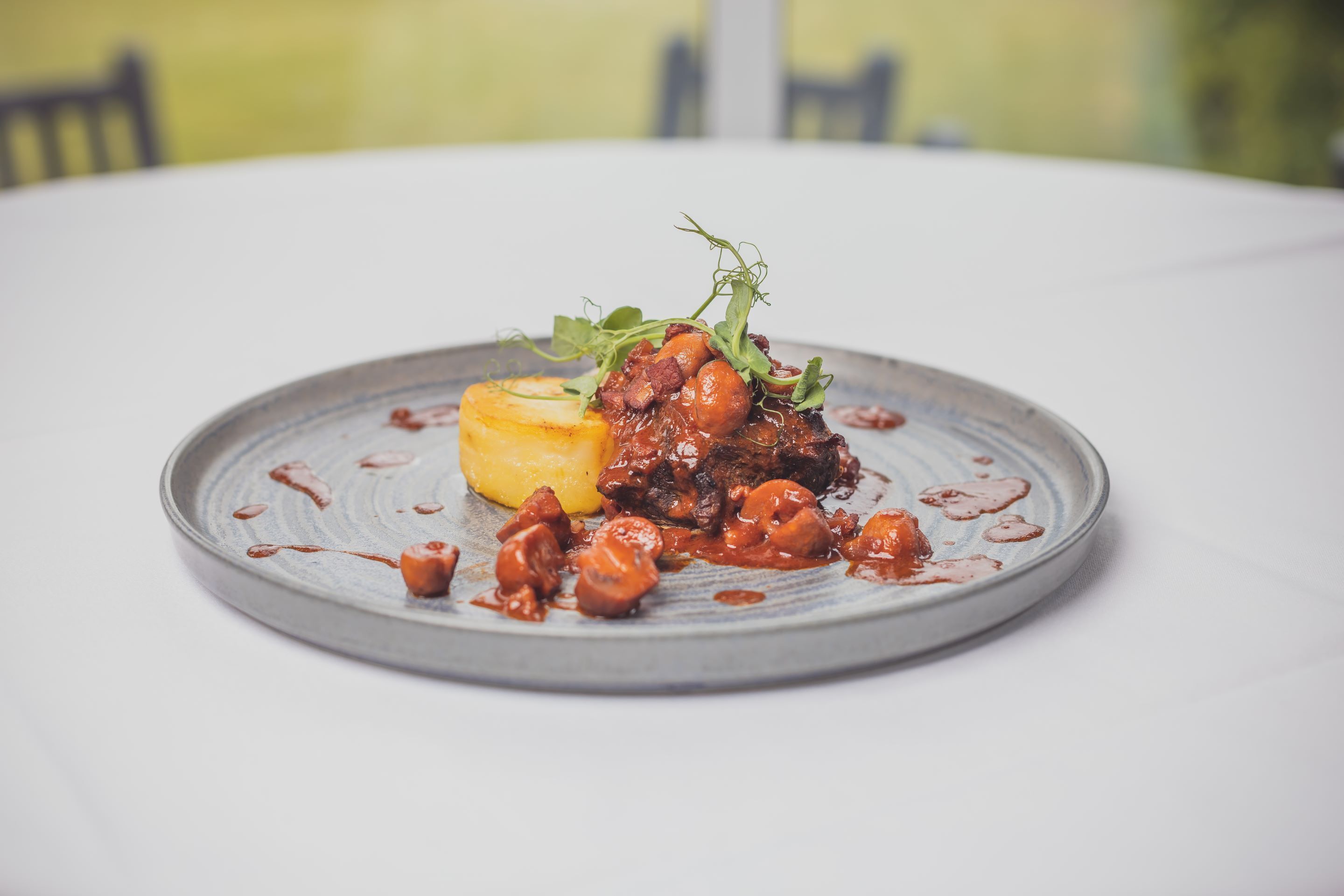 A plate of food with a meat dish, potatoes, and greens on a white table.
