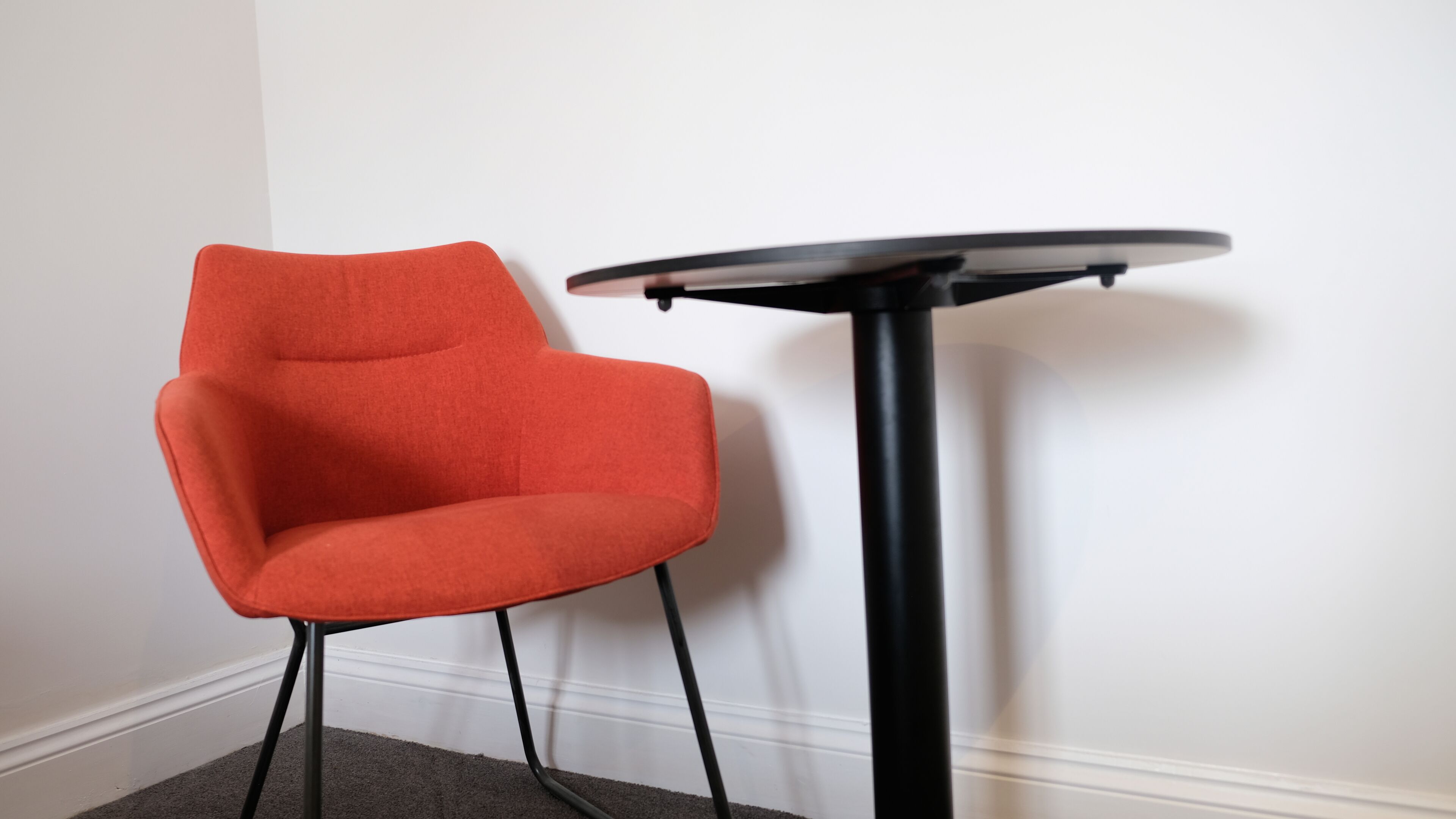 Une chaise rouge et une petite table noire adossées à un mur blanc.